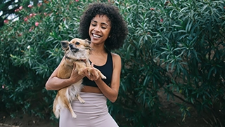 young woman in athletic wear holding small dog outside