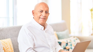 older white man wearing button down with laptop looking at personal insurance information in living room