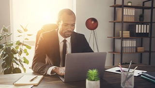male independent insurance agent wearing suit and tie on laptop at desk in business office male independent insurance agent wearing suit and tie on laptop at desk in business office