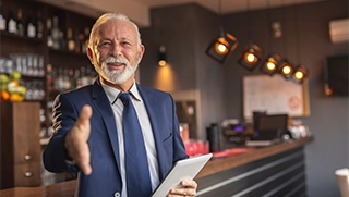 white male insurance agent with white beard wearing blue suit and tie in restaurant holding out hand to shake white male insurance agent with white beard wearing blue suit and tie in restaurant holding out hand to shake