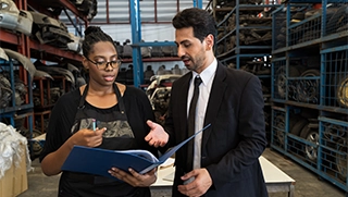 white male insurance agent wearing dark suit and tie speaking with black woman business owner in warehouse white male insurance agent wearing dark suit and tie speaking with black woman business owner in warehouse