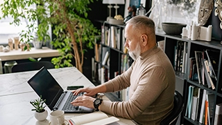 older white man with white beard on laptop in home office researching flood insurance coverage older white man with white beard on laptop in home office researching flood insurance coverage
