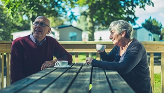 older couple with gray hair drinking coffee on picnic bench discussing insurance for their manufactured home in Florida