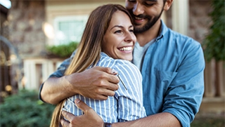 man and woman hugging in front of new home covered by affordable homeowners insurance policy