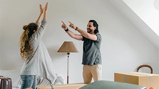 woman and man unpacking inside Florida apartment with arms raised and happy