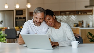 man and woman couple sitting at kitchen table on laptop researching insurance for their rental properties