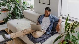 young black man sitting on couch in Florida apartment researching renters insurance on laptop