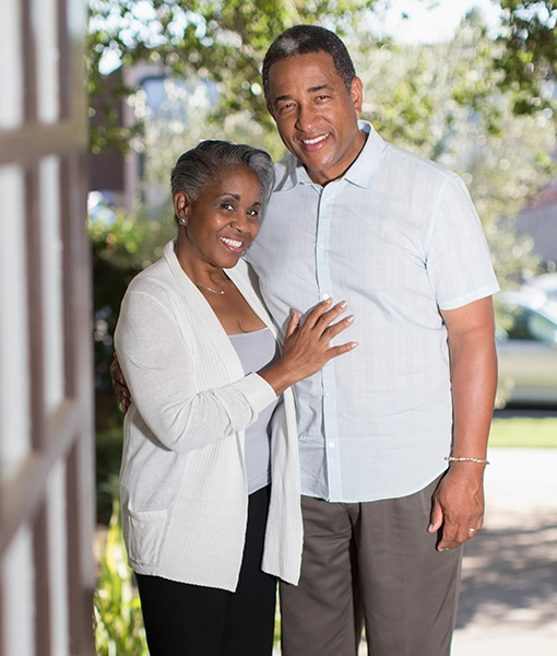 happy man and woman standing in front door with green trees in background